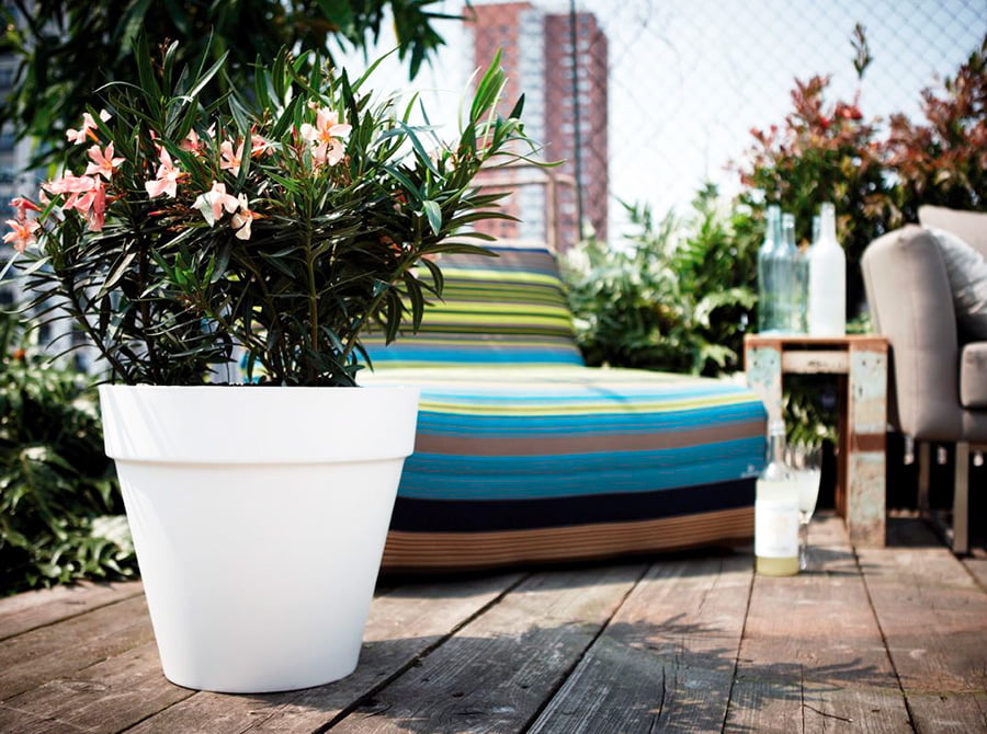 En esta terraza con suelo de madera hay un macetero grande de color blanco con flores. También un sofá bastante cómodo.